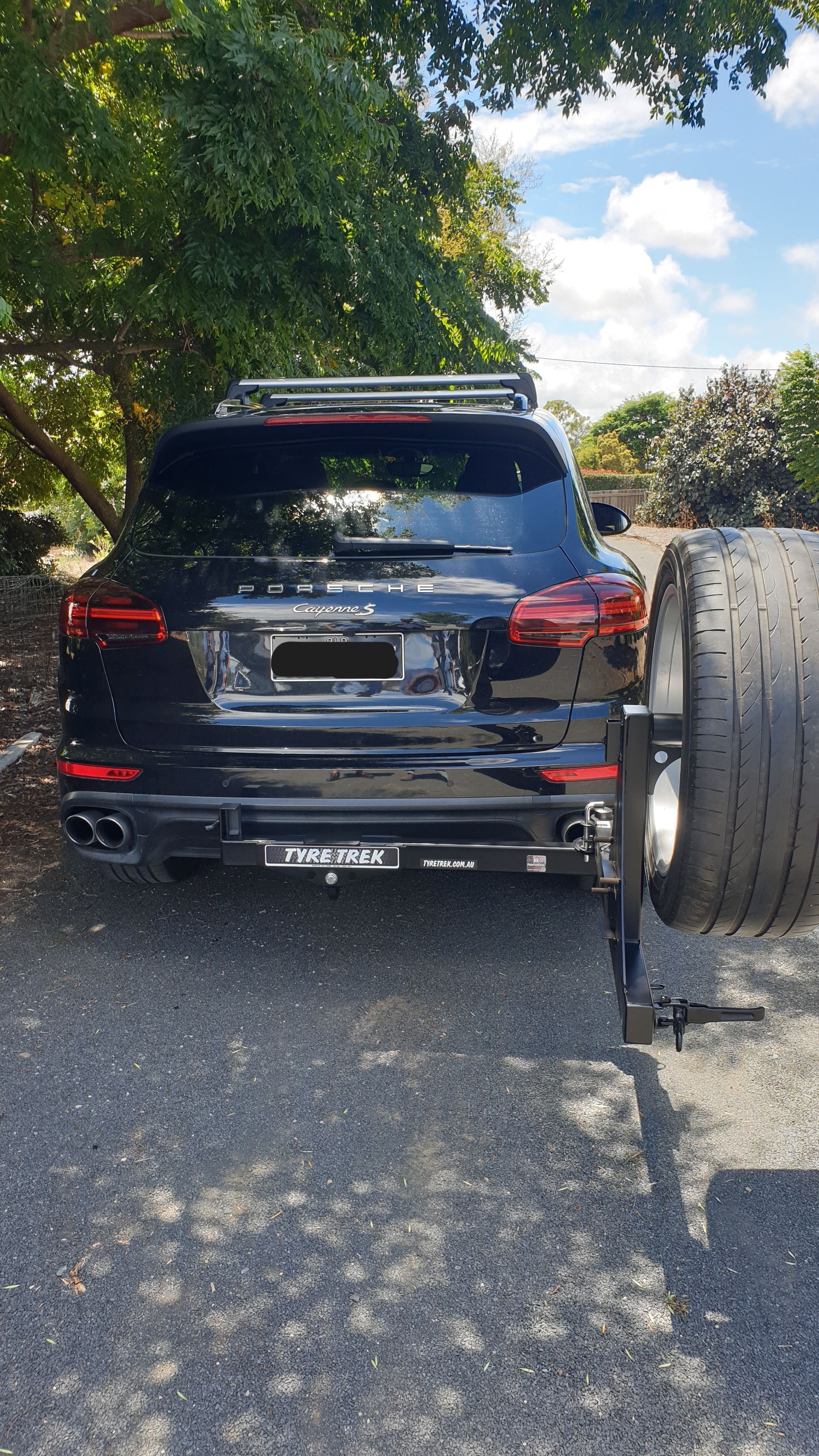 A black 4wd is parked on the side of the road with a tyre rack on the back.