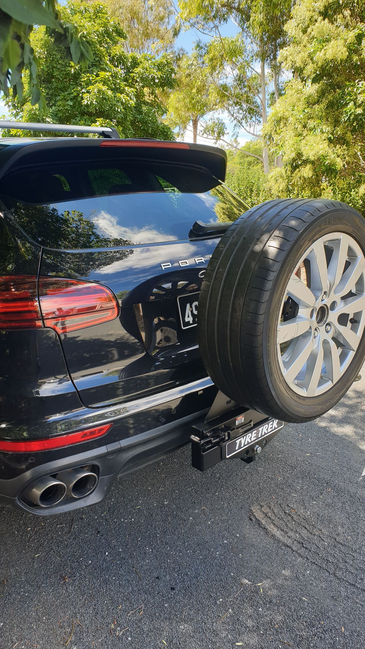 A black porsche cayenne with a spare tyre attached to the back of it is parked on the side of the road.