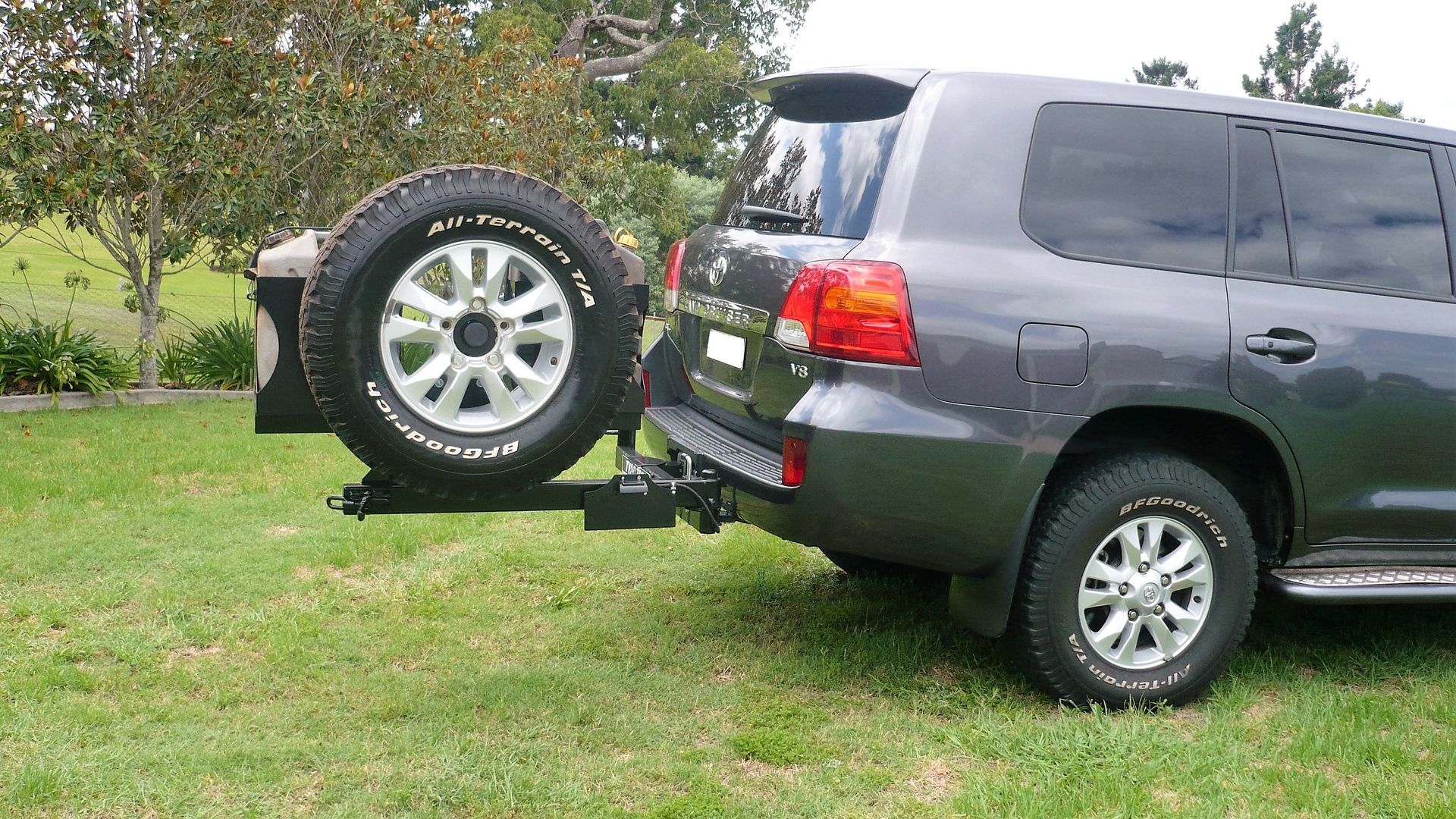 A suv with a tyre rack attached to it is parked in the grass.