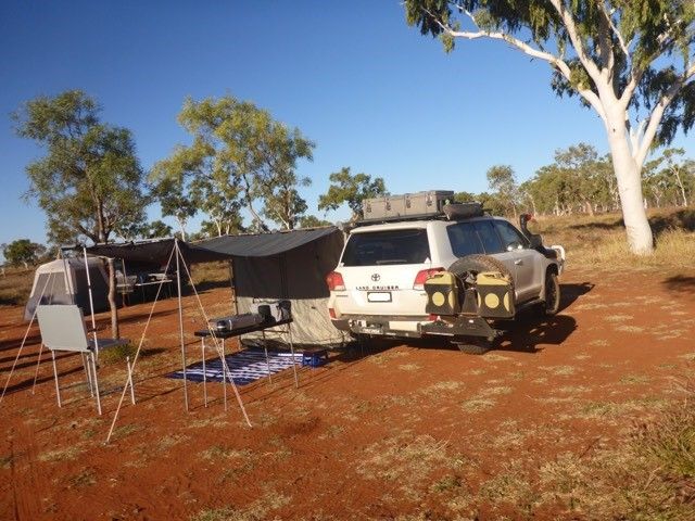A 4wd with a tyre rack attached to it is parked in a dirt field