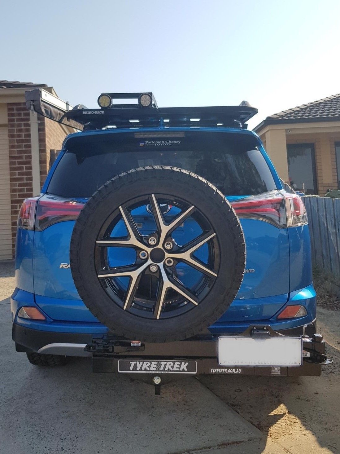 A blue suv with a spare tyre on the back is parked in a driveway.