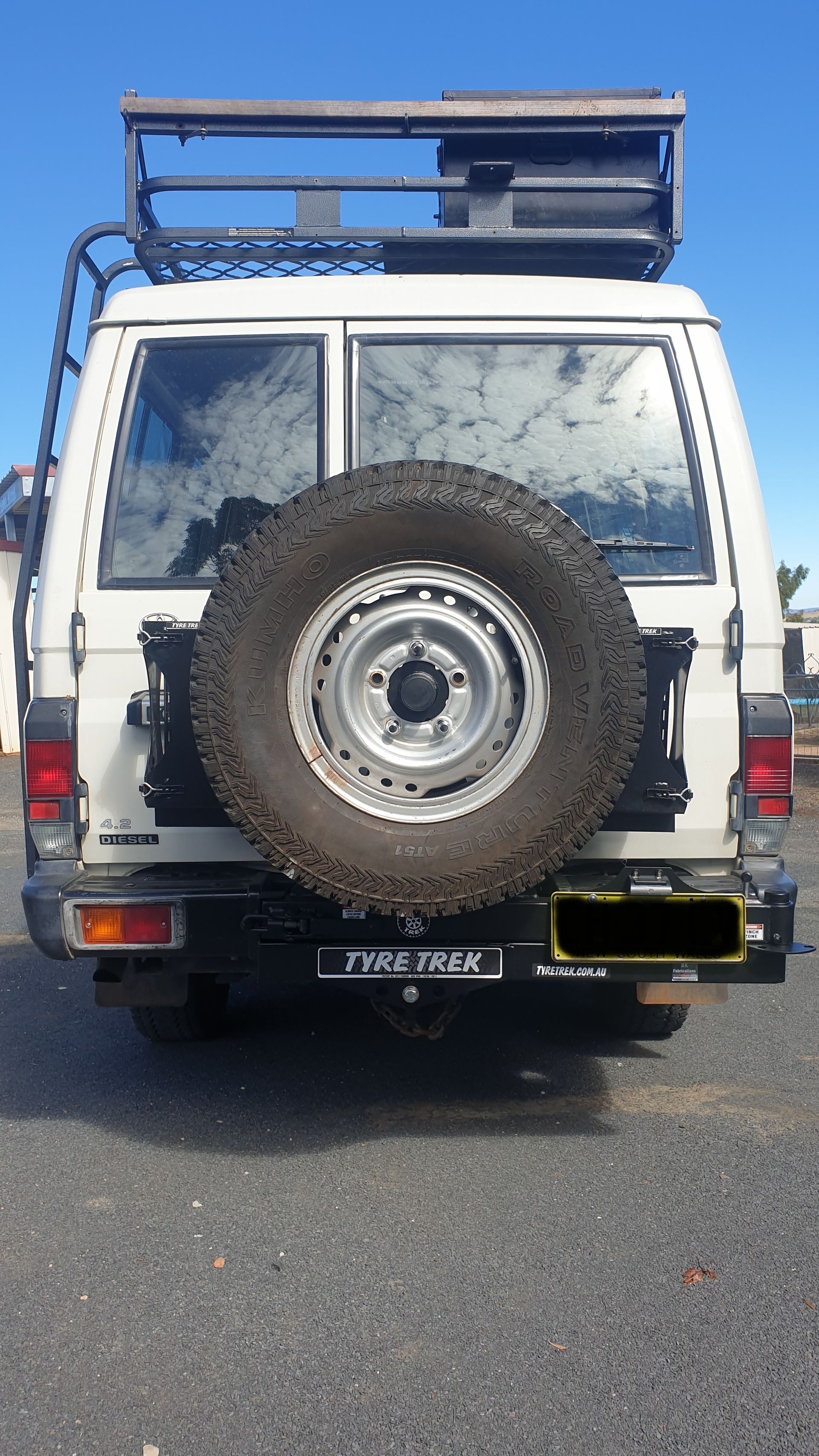 A white suv with a spare tyre on the back is parked in a carpark.