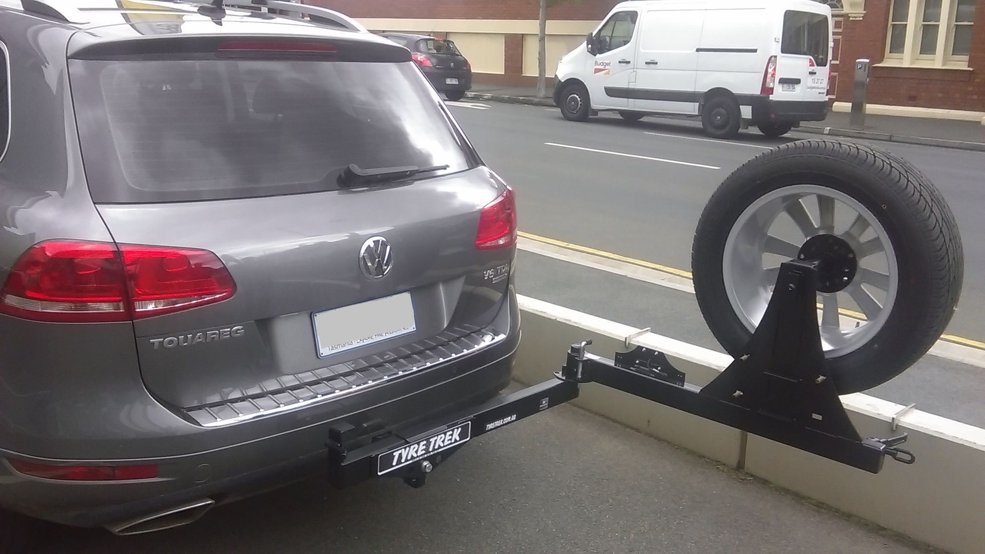 A volkswagen touareg is parked on the side of the road next to a white van.
