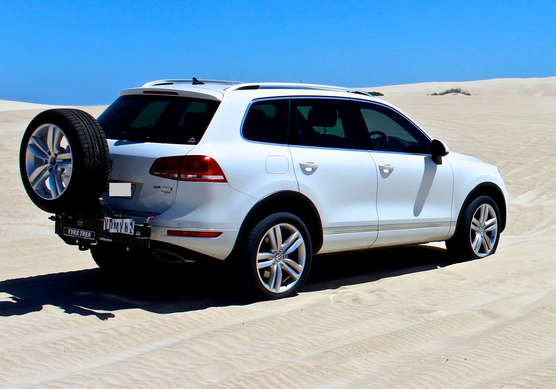 A white suv with a spare tyre on the back is parked in the sand