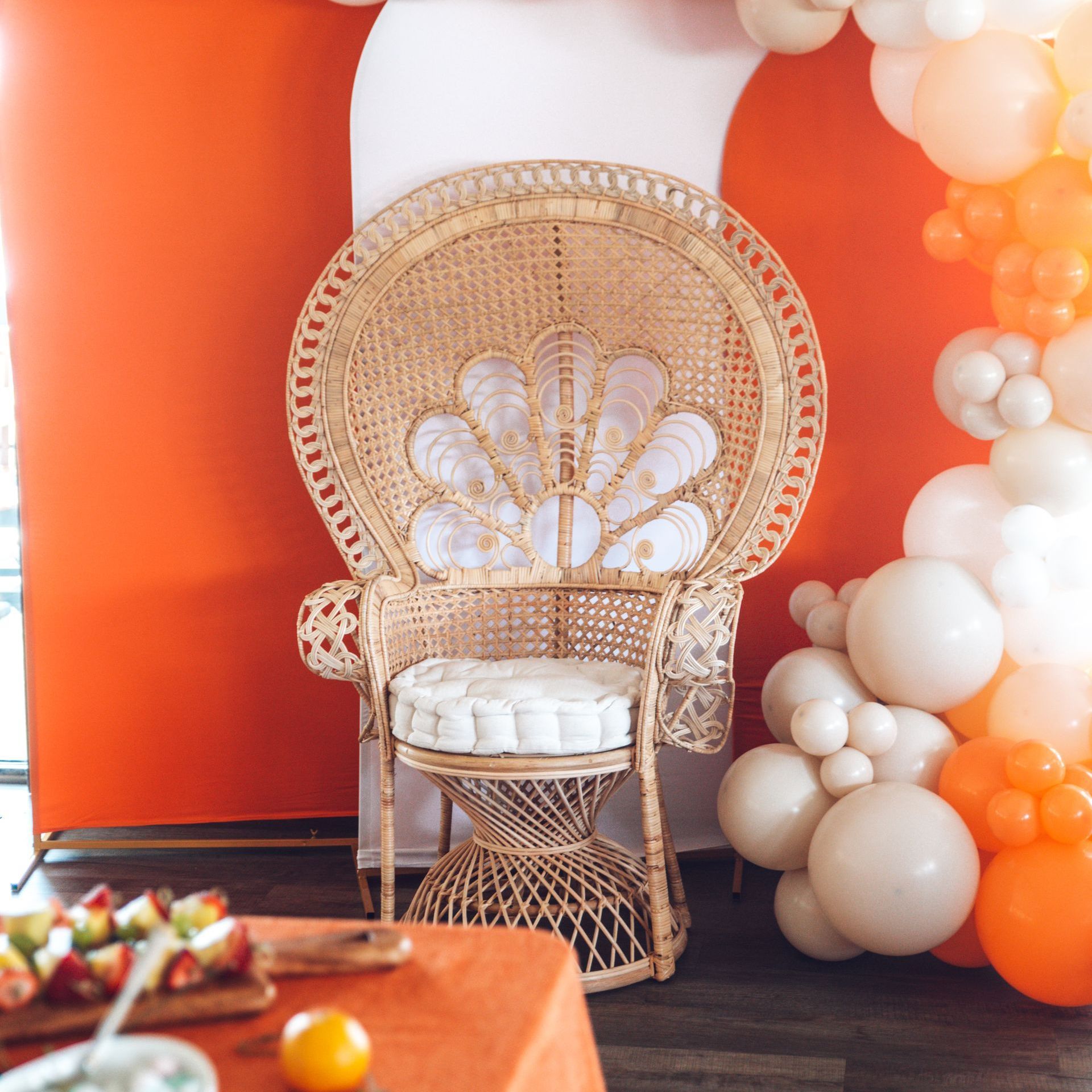 Rattan peacock chair on orange backdrop with balloons