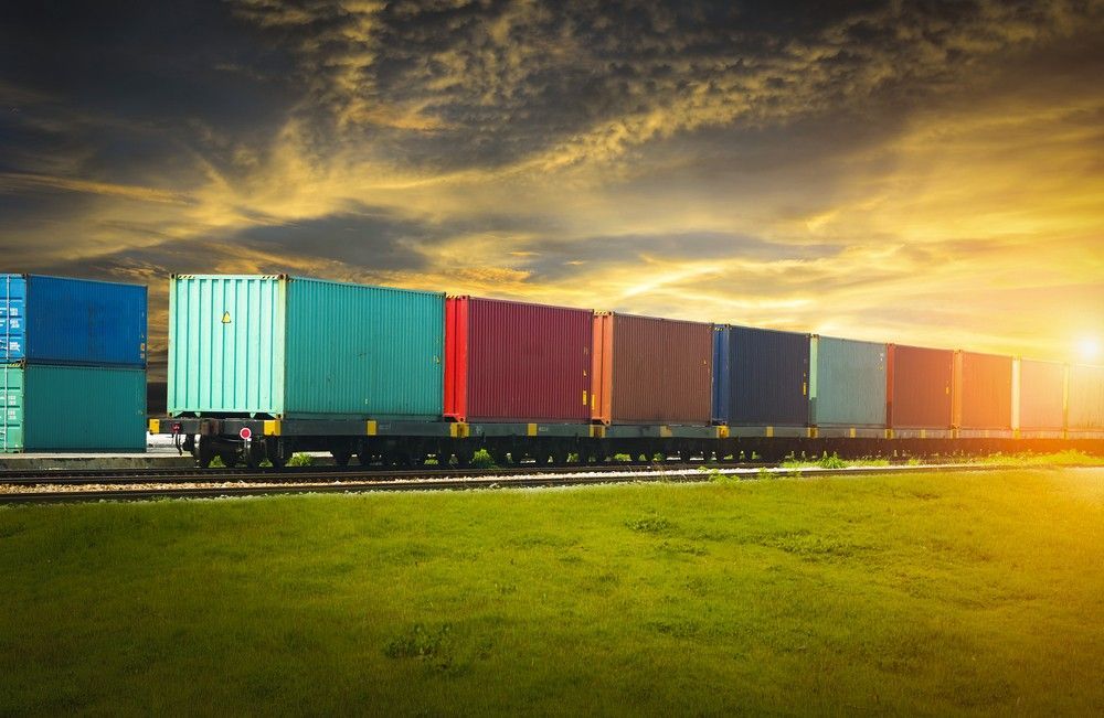 A train filled with containers is going down the tracks at sunset.