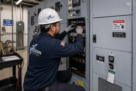 Technician in white hard hat inspecting electrical control panel in industrial room