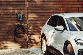 White SUV parked beside a wooden wall with a hose reel in warm sunlight