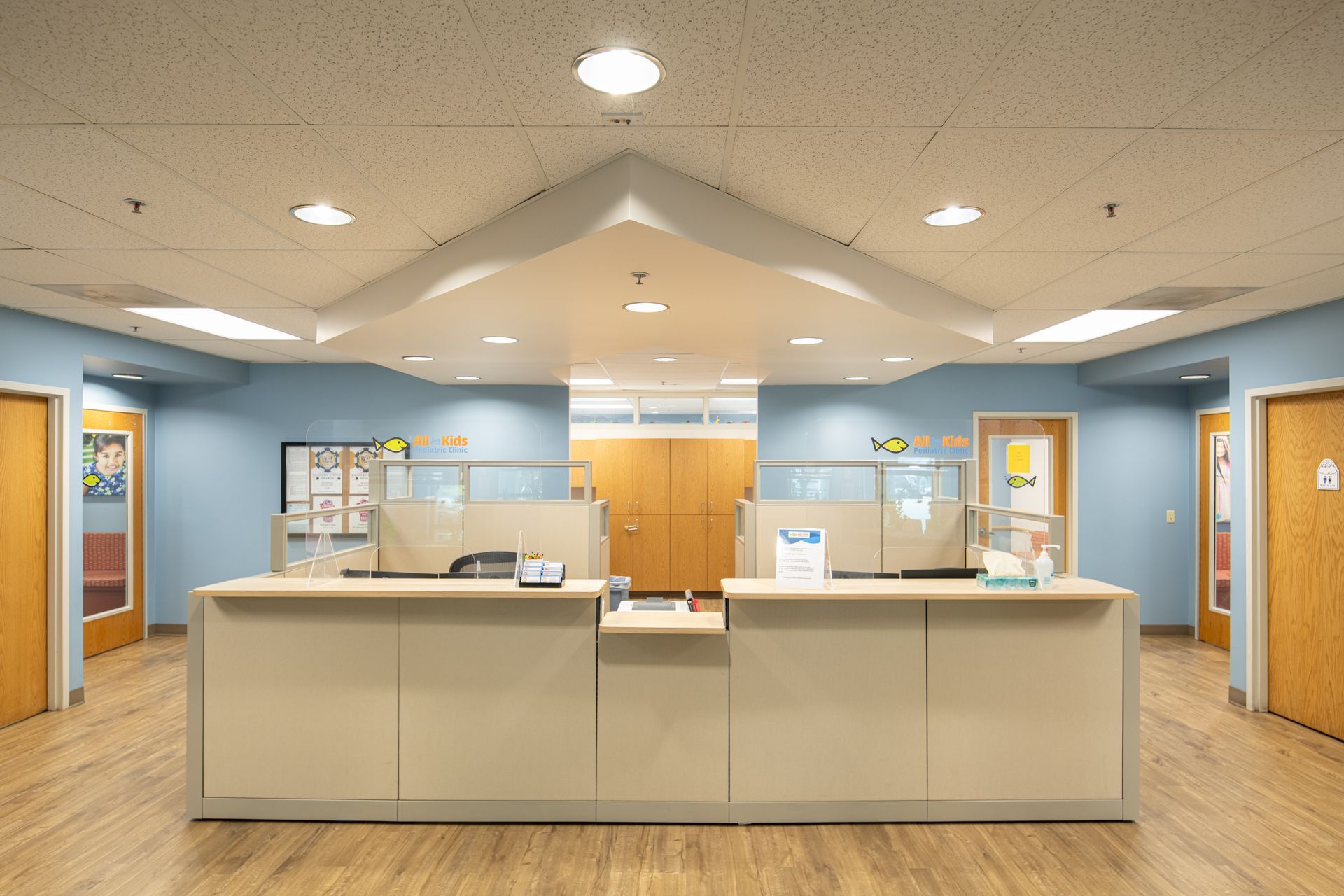 Reception area with light blue walls, tan desk, and wooden floors. Doors line the walls.