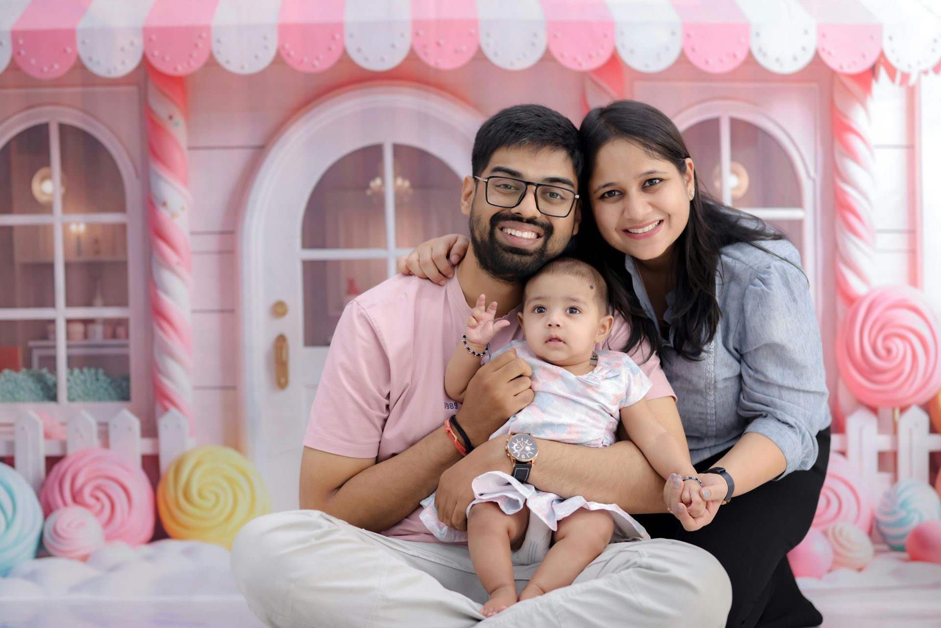 Family of three posing in front of a candy-themed backdrop: father, mother, and baby.