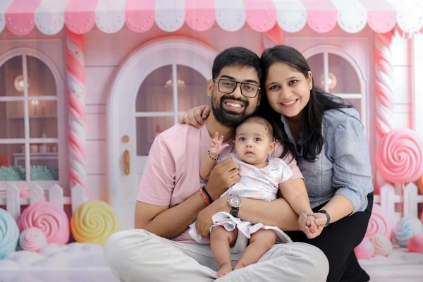 Family of three smiling, posing in front of a pink candy-themed backdrop.