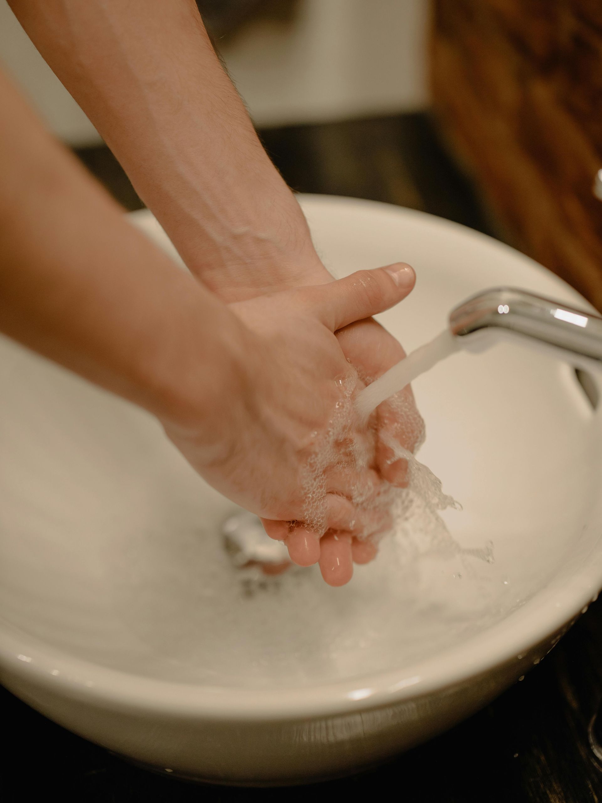 Person washing hands in a white sink under running water.