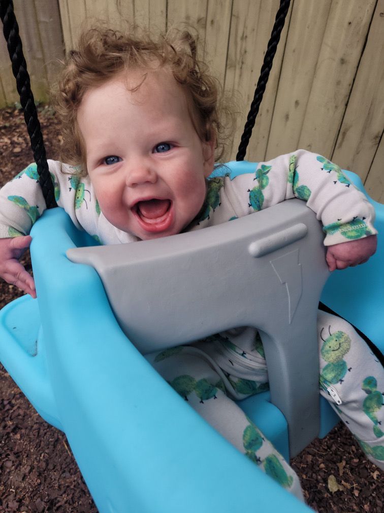 A baby on their stomach on a white surface, smiling at colorful toys outdoors.