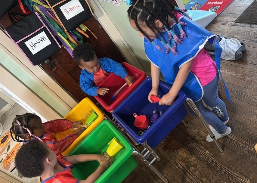 Children gather around a white table, drawing and creating colorful crafts with paper, markers, and scissors.