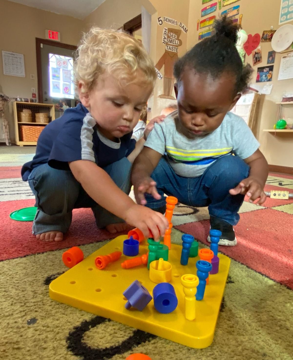 Children and a teacher playing with colorful building blocks on a rug in a playroom.