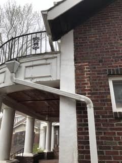 A brick house with a balcony and a gutter on the side of it.