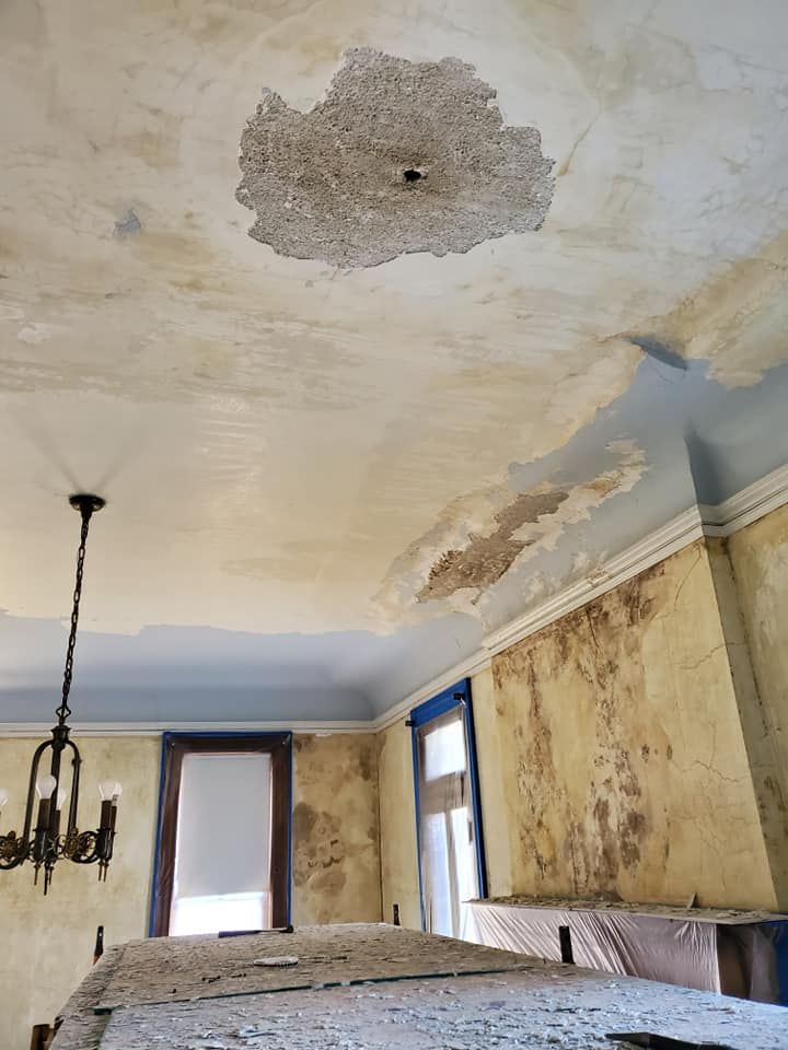 A room with a ceiling that is peeling and a chandelier hanging from it.