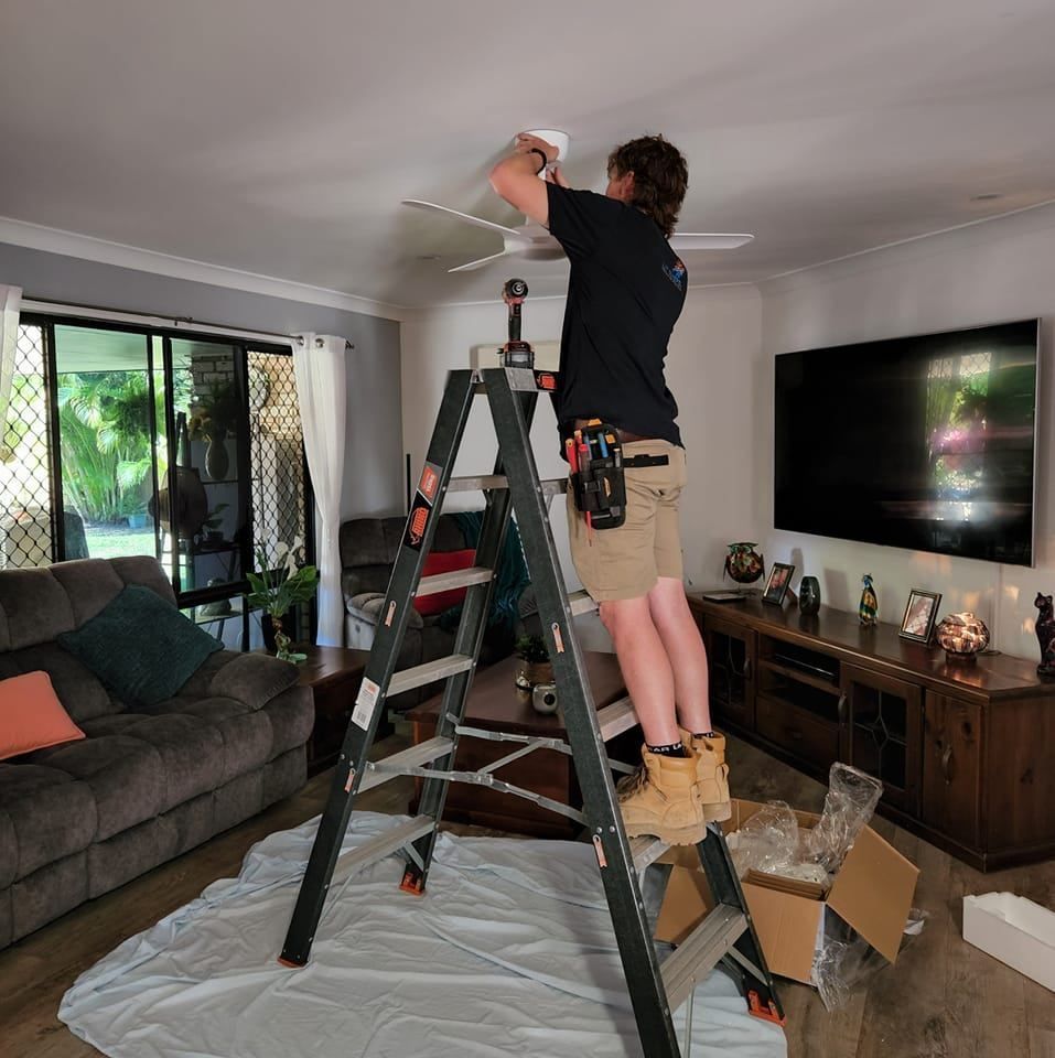 Man On Ladder Installing A Ceiling Fan In A Living Room — Lit Energy in Seaforth, QLD