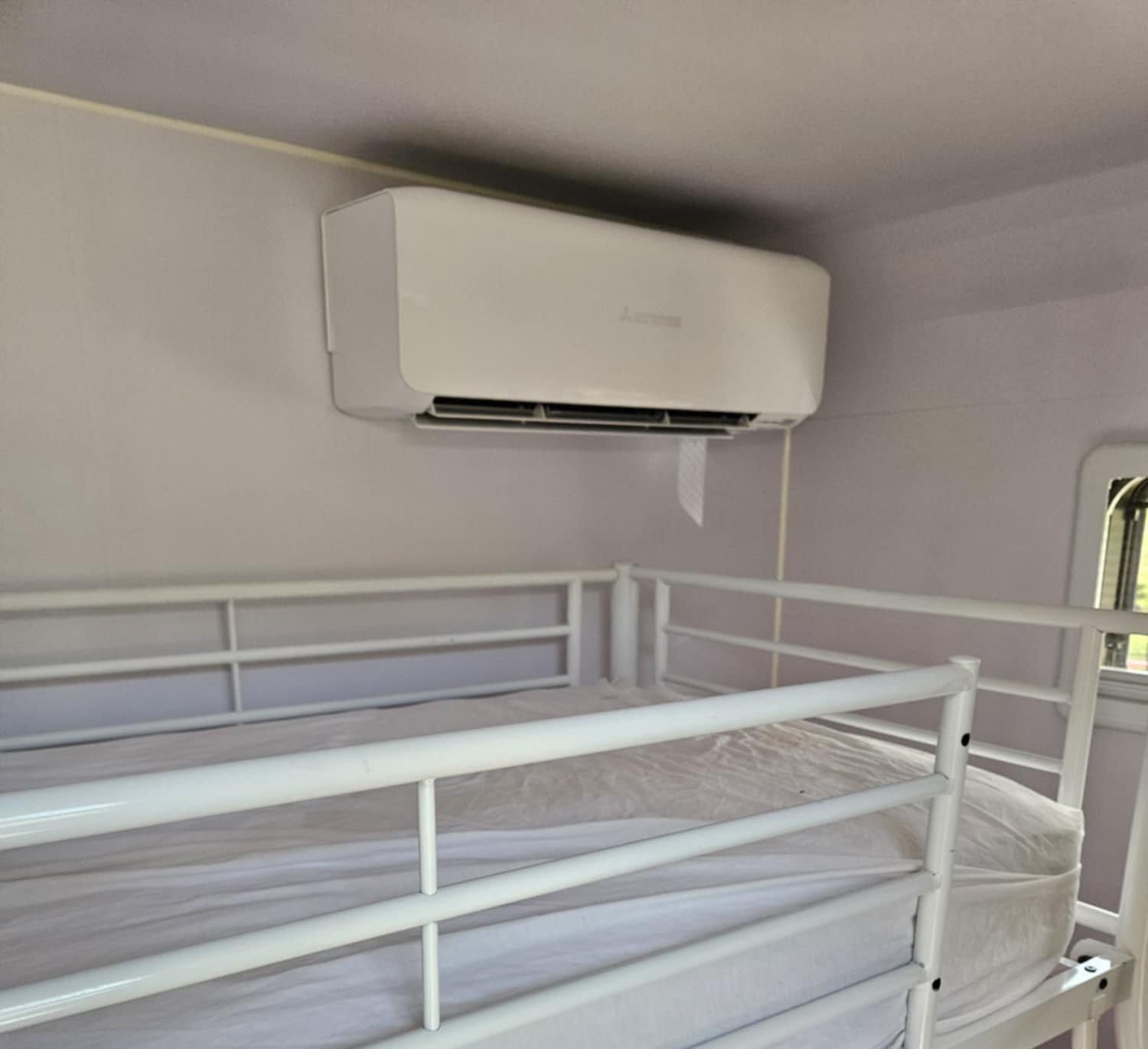 White Bunk Beds In A Room With A White Air Conditioner Mounted On The Wall Above The Top Bunk — Lit Energy in Seaforth, QLD