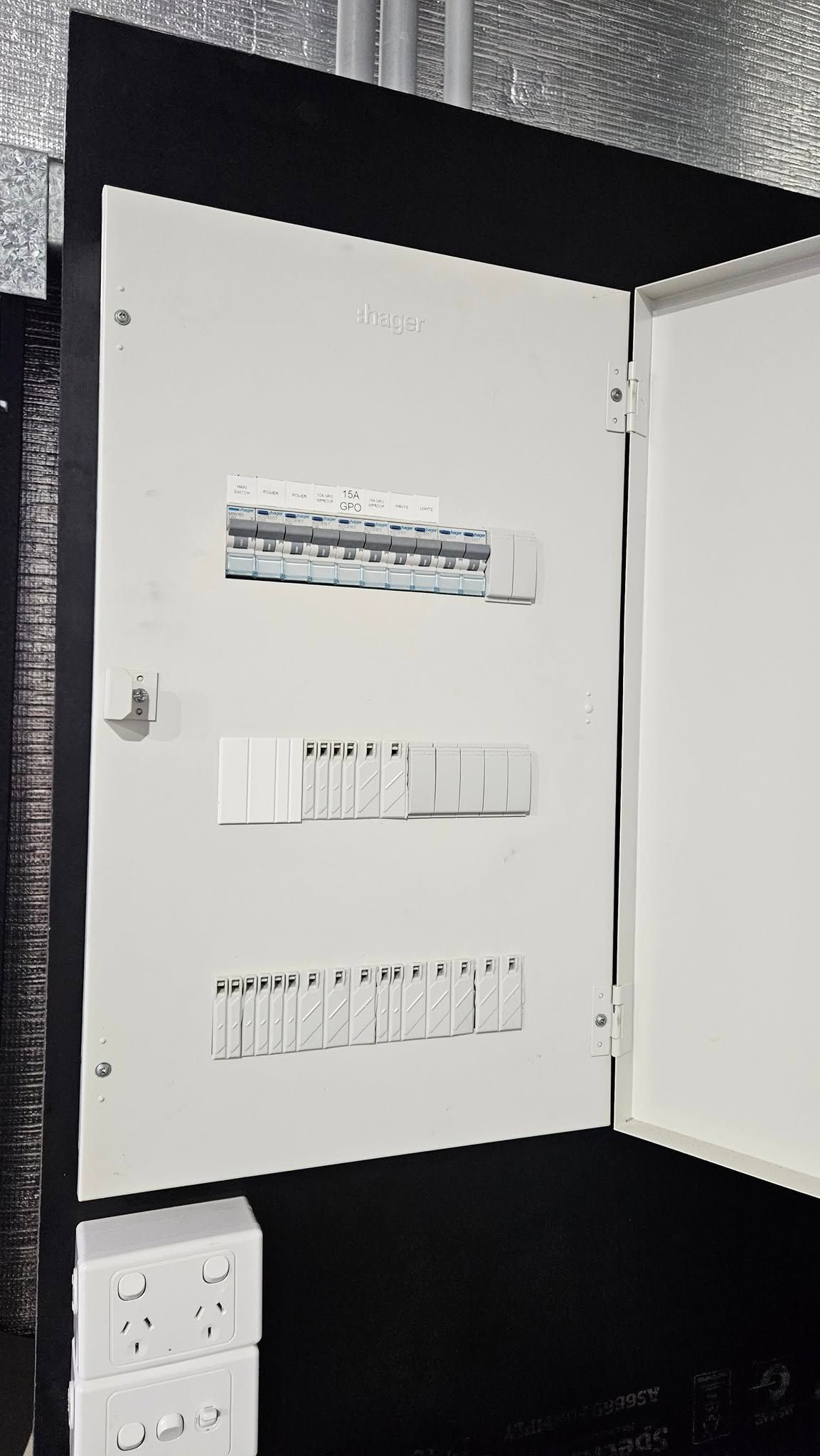 Electrical Panel With Open Door, White Interior, Installed On A Dark Wall With Power Outlets Below — Lit Energy in Seaforth, QLD