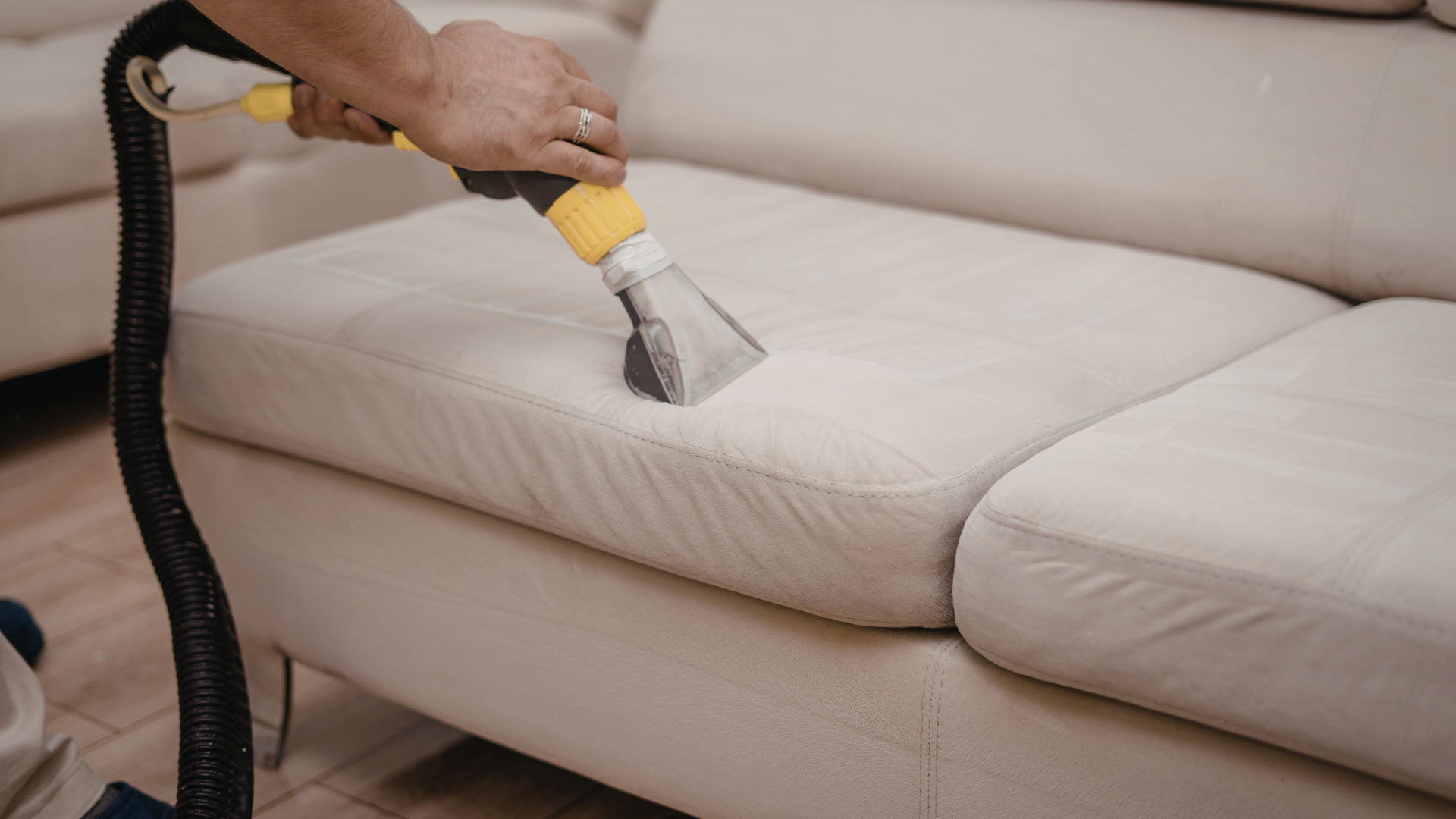 Person cleaning a light-colored sofa with a handheld upholstery cleaner.