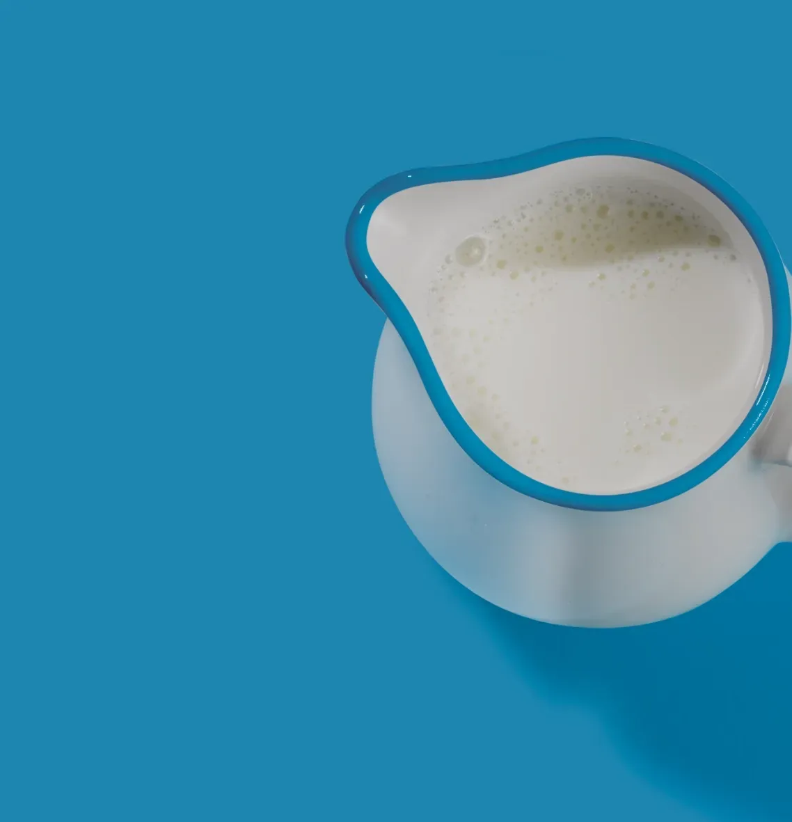 A pitcher of milk sits on a blue surface