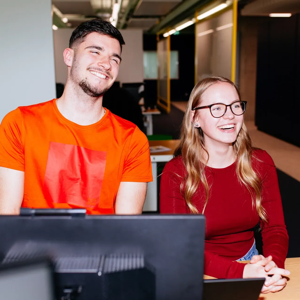 A man and a woman are sitting in front of a computer and smiling