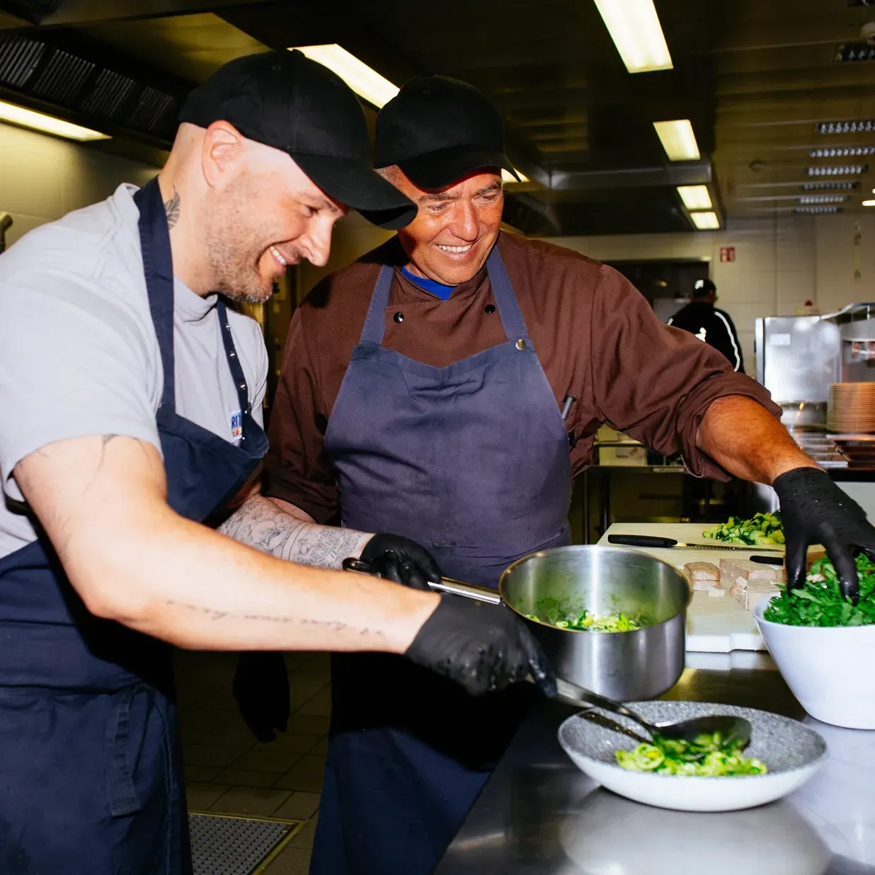 Two men in aprons are preparing food in a kitchen