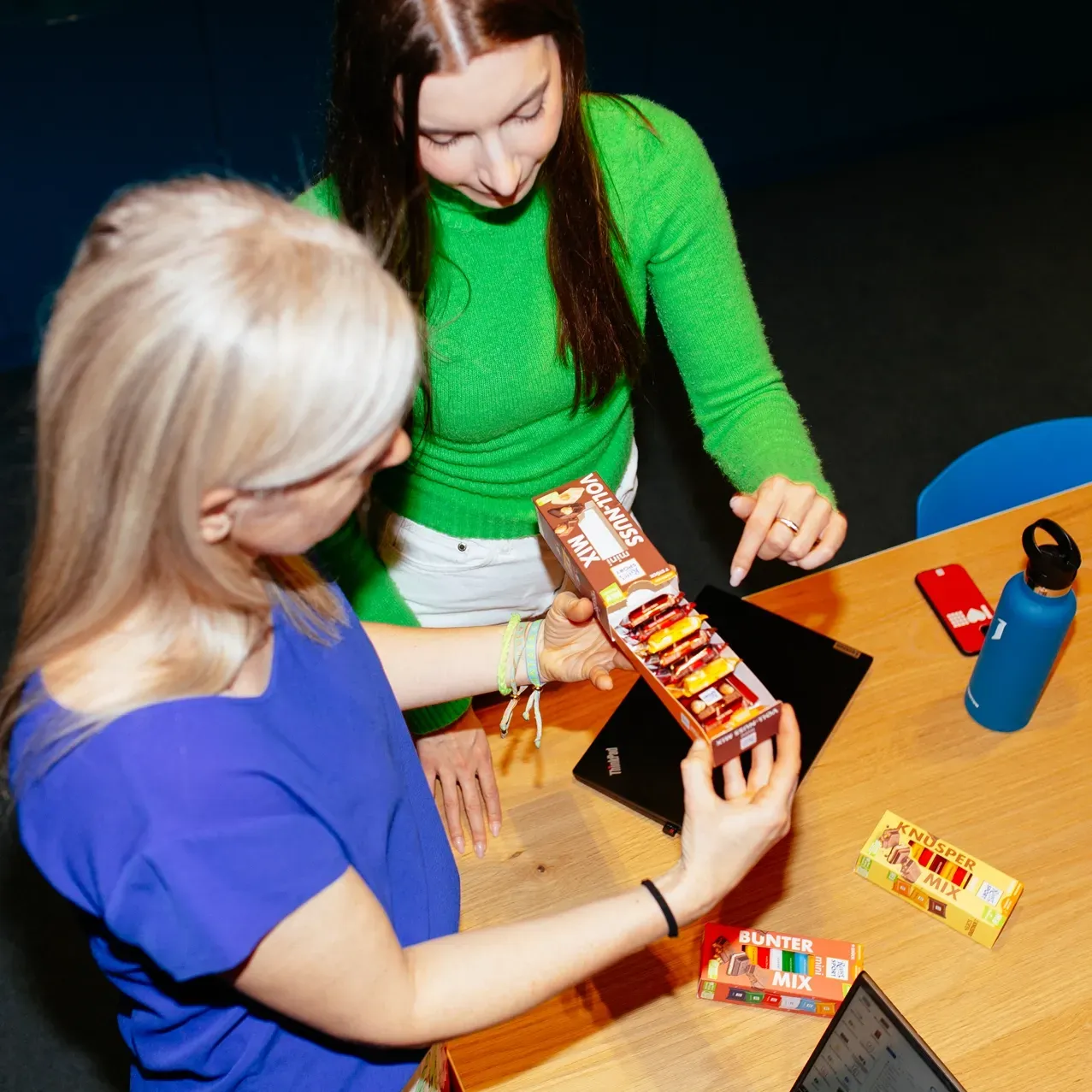 Two women are sitting at a table looking at a box of Ritter Sport