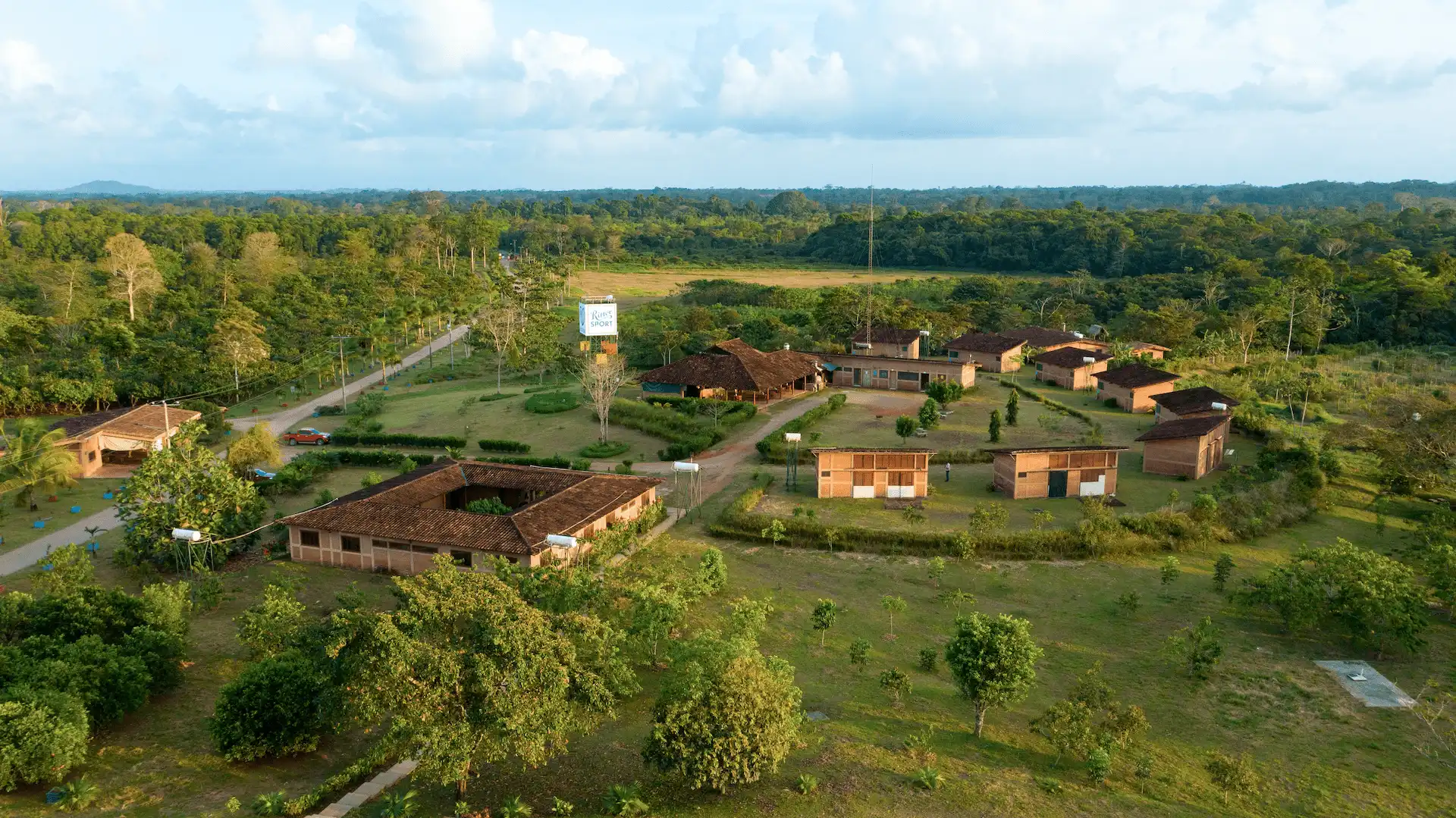 Aerial view of a rural compound with several buildings surrounded by trees and green fields.