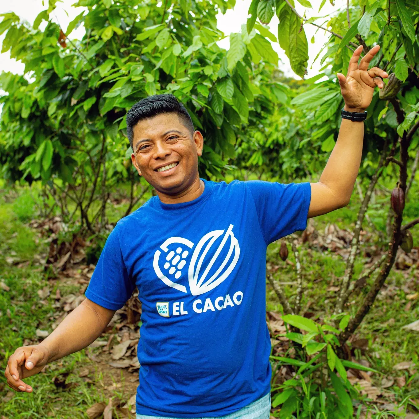 A man wearing a blue shirt that says el cacao on it, smiling in the camera
