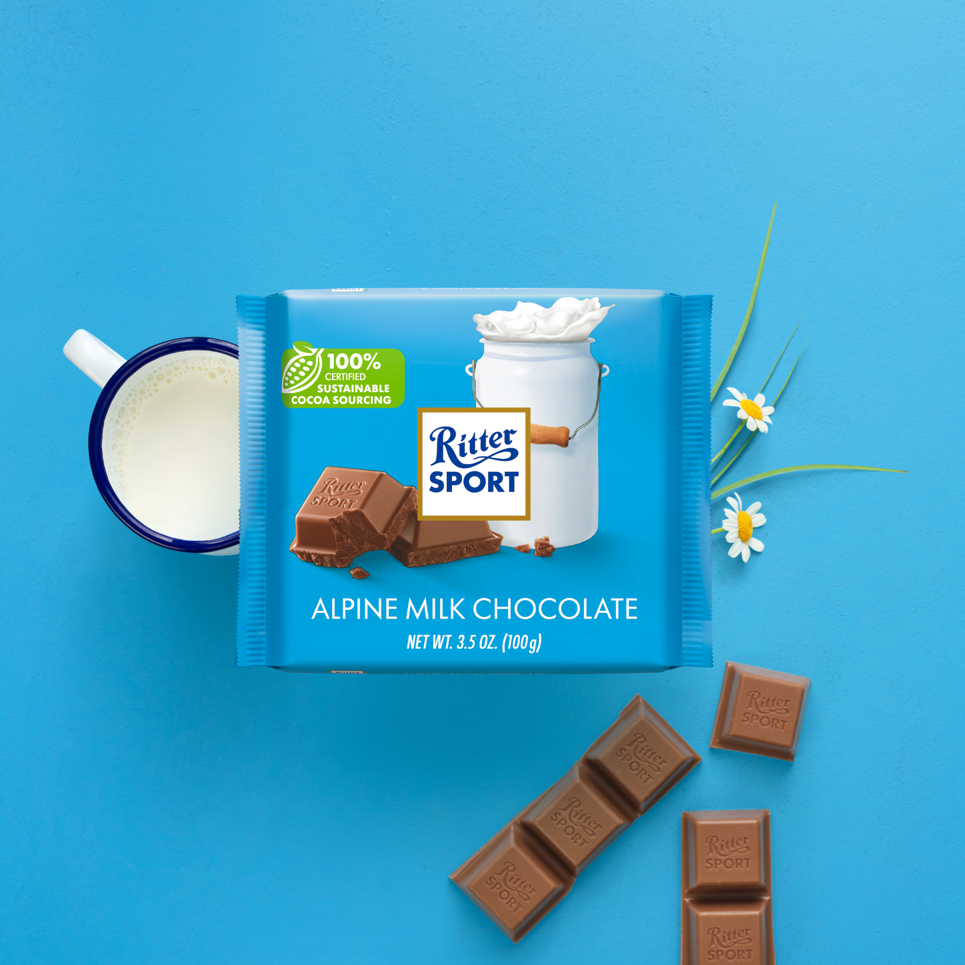 Ritter Sport Alpine Milk Chocolate bar on blue surface with milk cup and daisies.