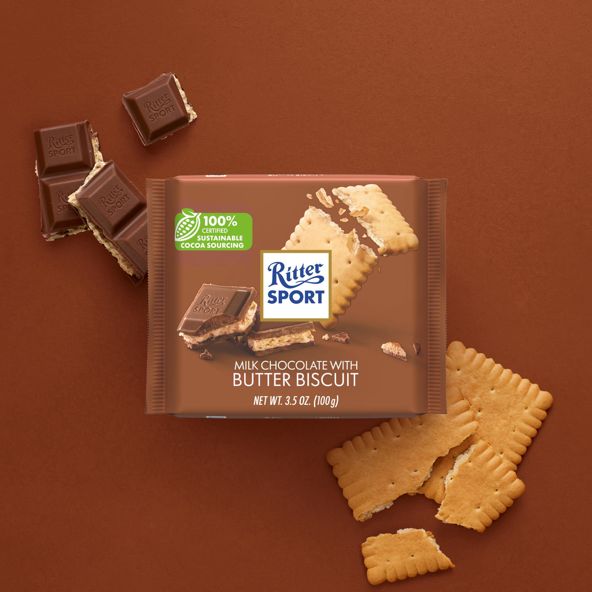 Ritter Sport Milk Chocolate with Butter Biscuit bar packaging with scattered chocolate pieces and biscuits on a brown background.