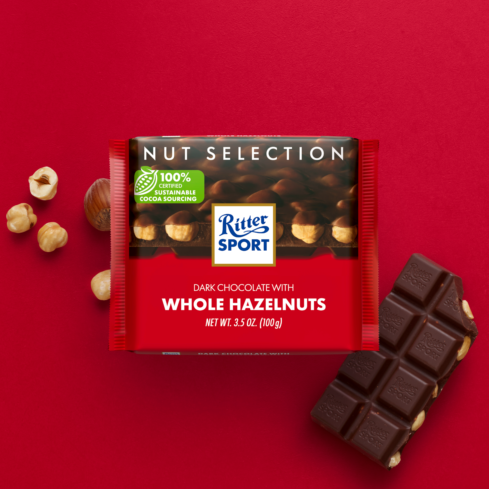 Ritter Sport dark chocolate bar with whole hazelnuts on a red background with loose nuts and broken pieces.
