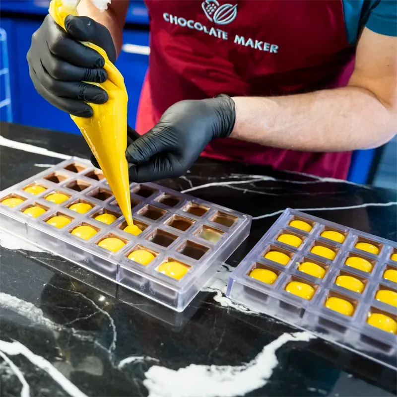Schokoladenpralinen werden mit einer Spritztüte mit einer gelben Füllung per Hand gefüllt.