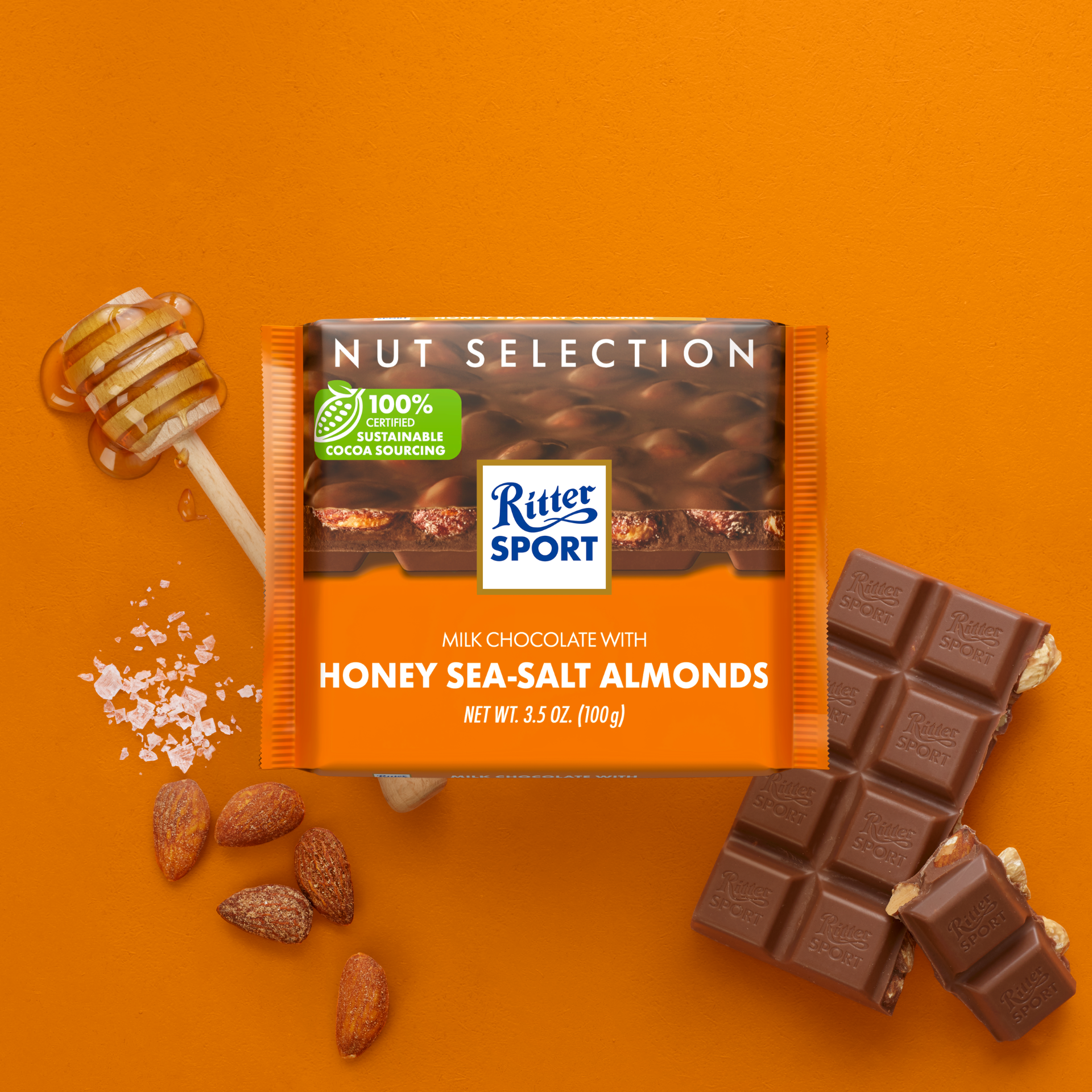 Ritter Sport Nut Selection bar. Milk chocolate with honey sea-salt almonds. Orange background with almonds and a honey stick.