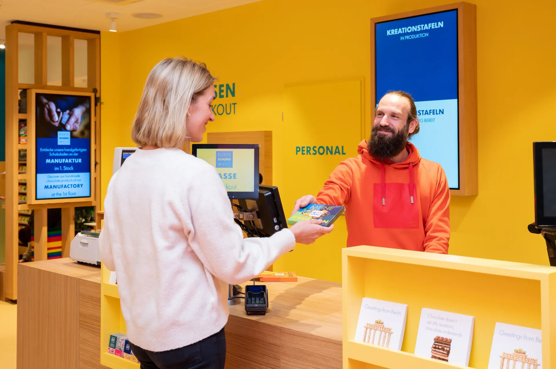 Ein Mann im orangefarbenen Sweatshirt gibt einer Frau eine Schokolade