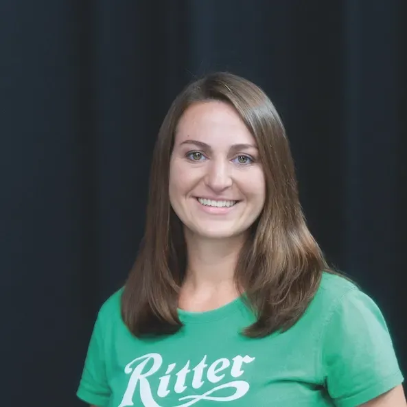 A woman wearing a green shirt with the Ritter Sport Logo on it is smiling.