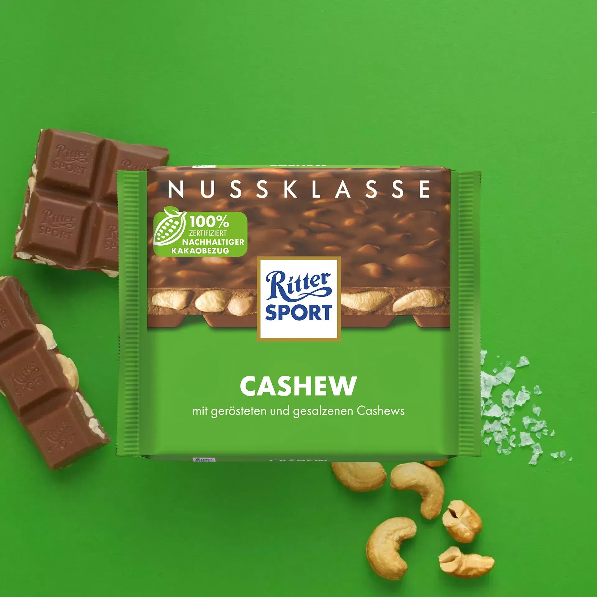 Ritter Sport Cashew chocolate bar with scattered cashews, chocolate pieces, and a green background.