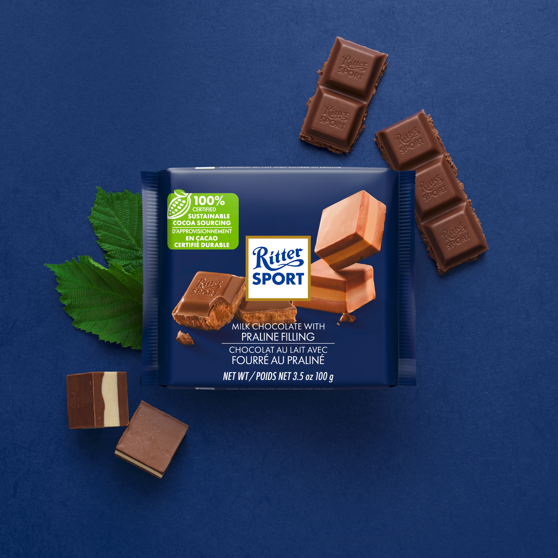 Ritter Sport chocolate bar with hazelnut filling on blue background, with detached chocolate squares and a leaf.