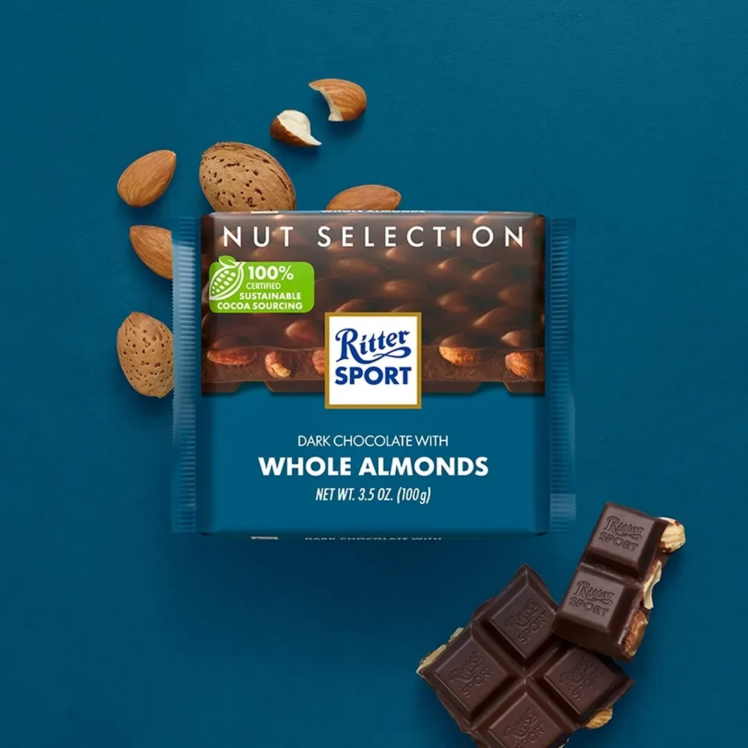 Ritter Sport chocolate bar with almonds on a blue surface, scattered almonds nearby, and a partially eaten bar.