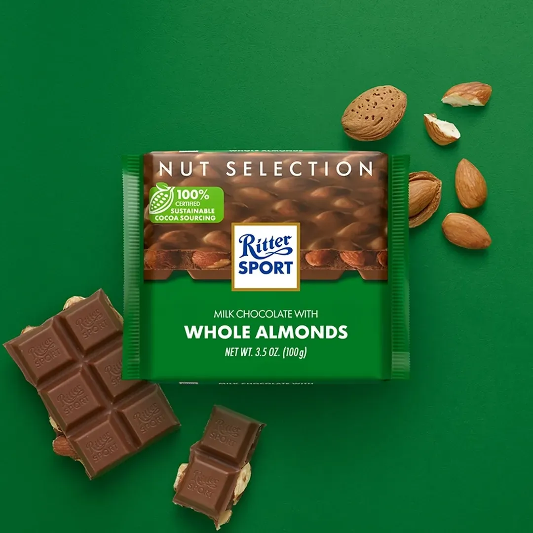 Ritter Sport chocolate bar with almonds on a blue surface, scattered almonds nearby, and a partially eaten bar.