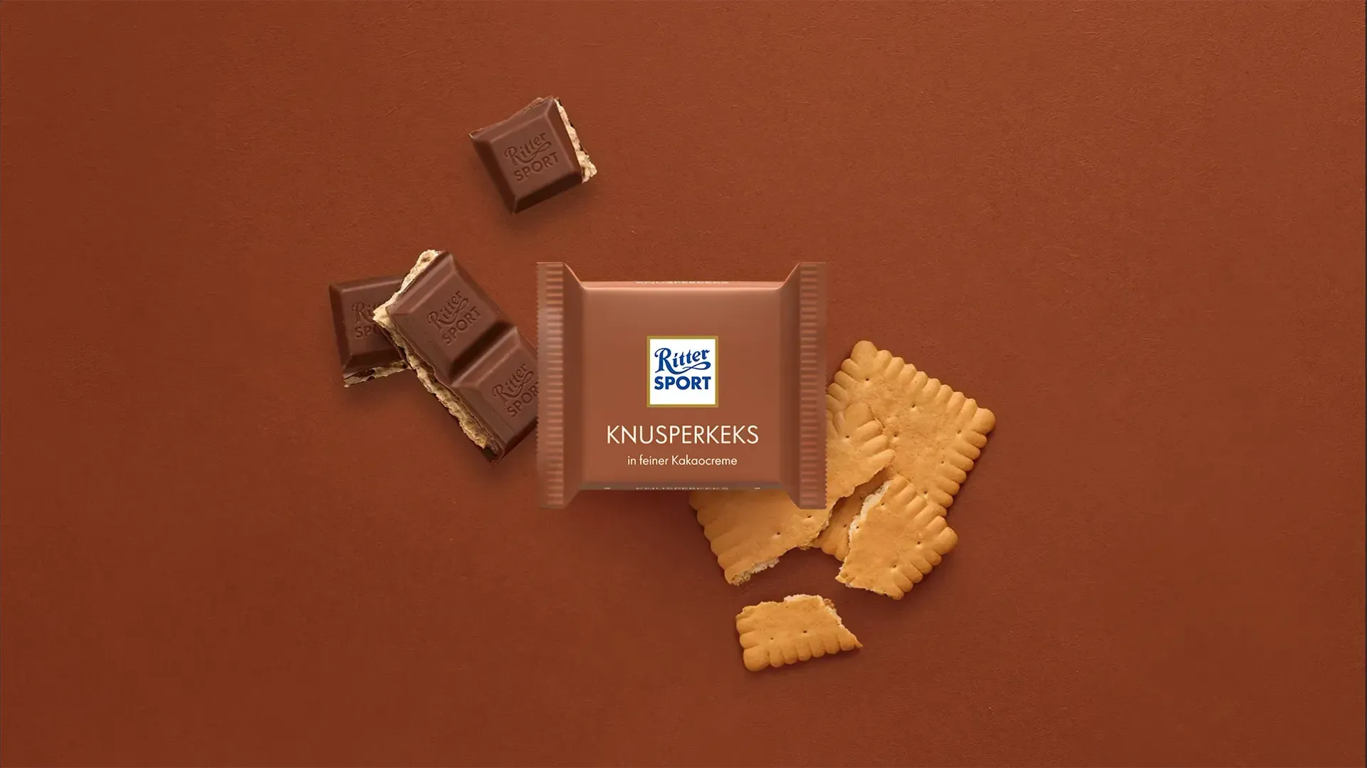 Verpackung einer blauen Schokoladentafel mit Nüssen, Schokoladenstückchen und dem Hinweis „55 % Kakaoanteil“ auf blauem Hintergrund