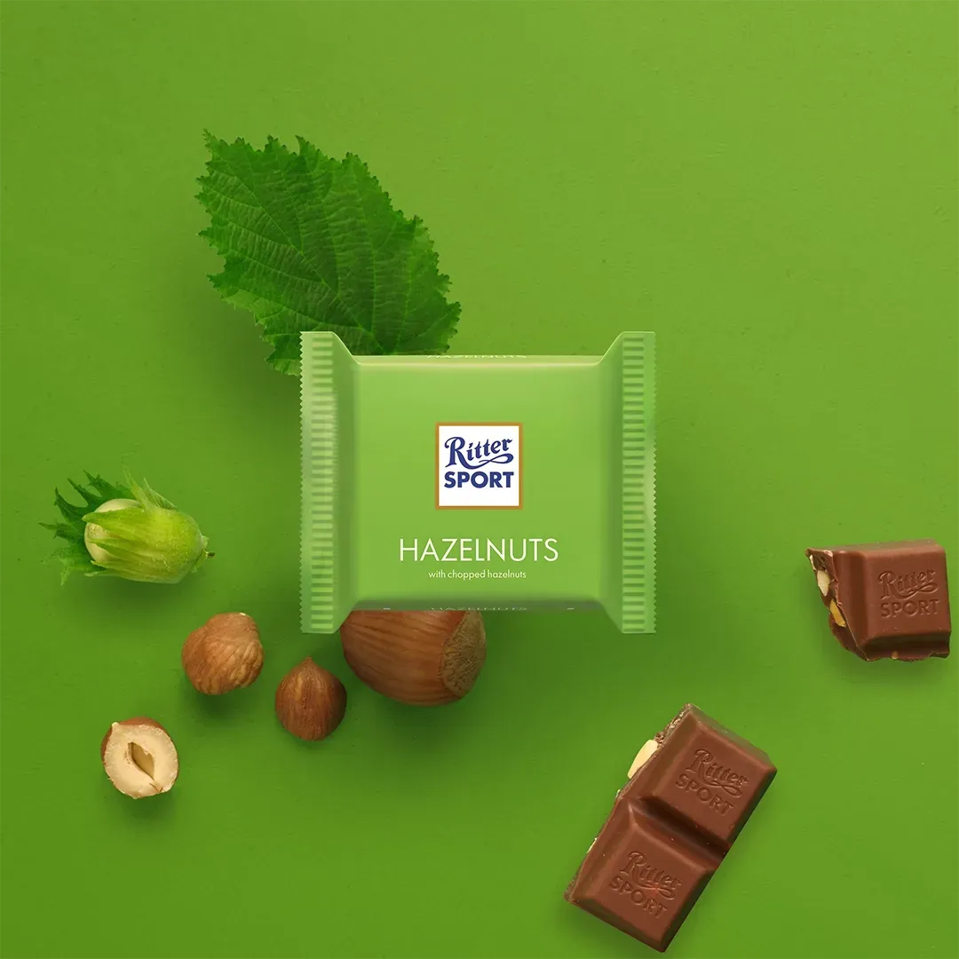 Green Ritter Sport Hazelnut chocolate bar with hazelnuts and leaf on green background.