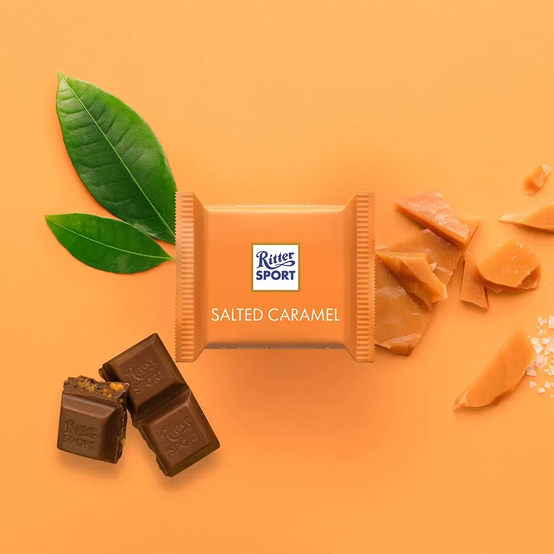 Ritter Sport salted caramel chocolate bar with caramel pieces, chocolate squares, and leaves on an orange background.