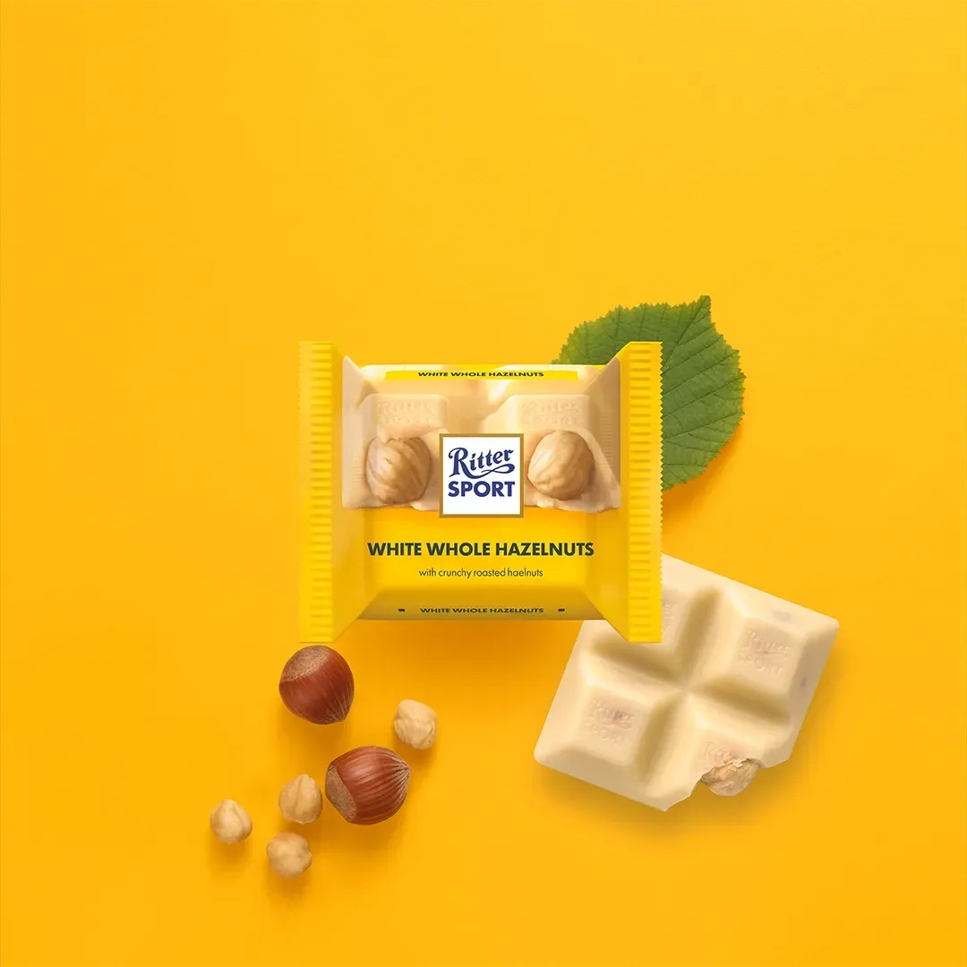 Ritter Sport chocolate bar with almonds on a blue surface, scattered almonds nearby, and a partially eaten bar.