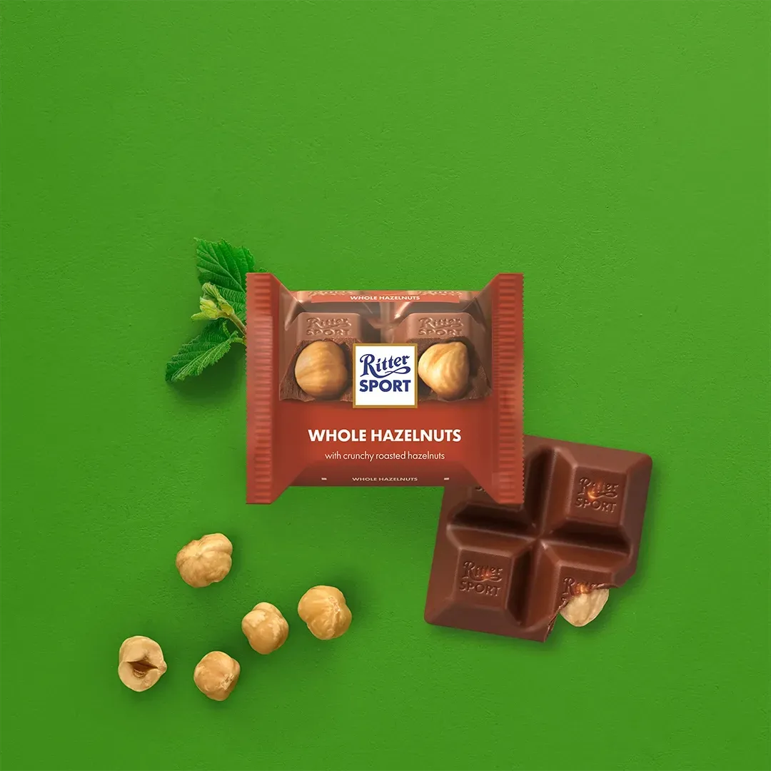 Ritter Sport chocolate with whole hazelnuts and unwrapped squares, green background.