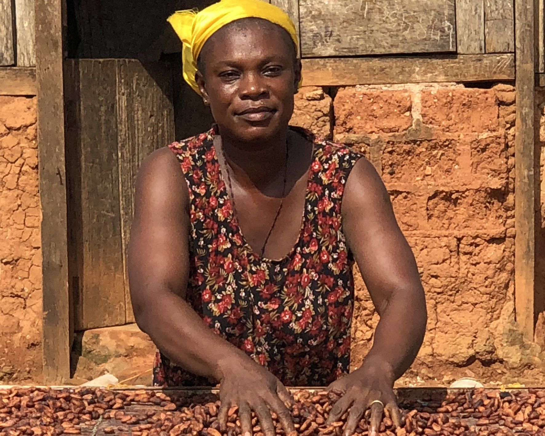 A woman wearing a yellow headband sits in front of a pile of cocoa beans