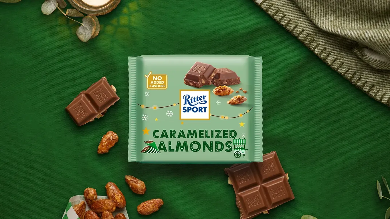 Ritter Sport chocolate bar packaging with cocoa beans, broken chocolate, and milk on a blue background.