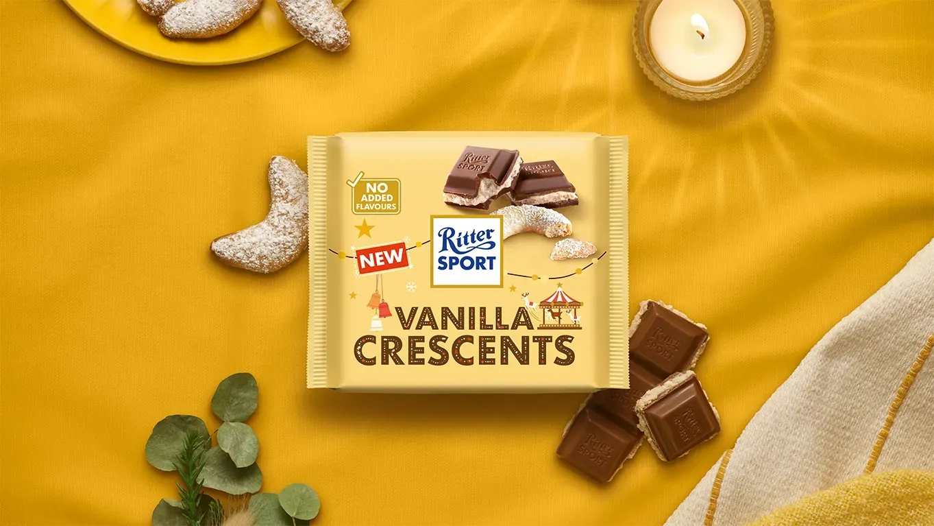 Ritter Sport chocolate bar packaging with cocoa beans, broken chocolate, and milk on a blue background.